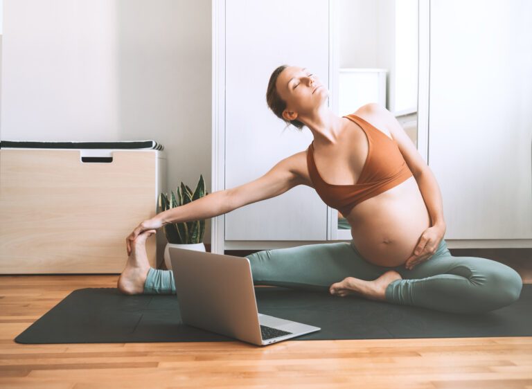 Pregnant woman practicing yoga at home with laptop. Expectant mother doing prenatal video training class indoors